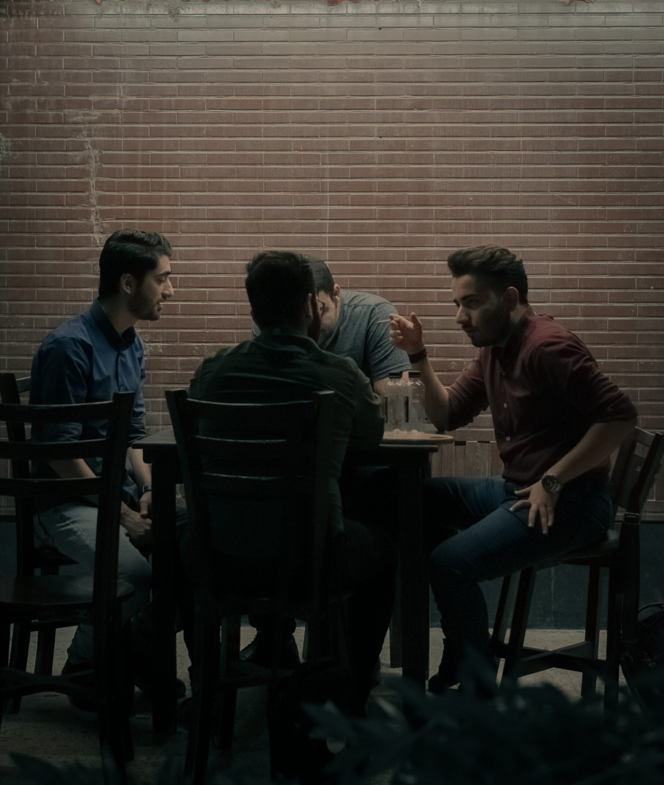 The photo is of four men sitting around a table. They are chatting together in a darkened corner.