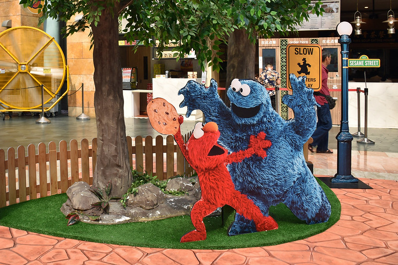 A photo of Sesame Street characters Cookie Monster and Elmo. Cookie Monster scares Elmo as Elmo holds on tight to his cookie.