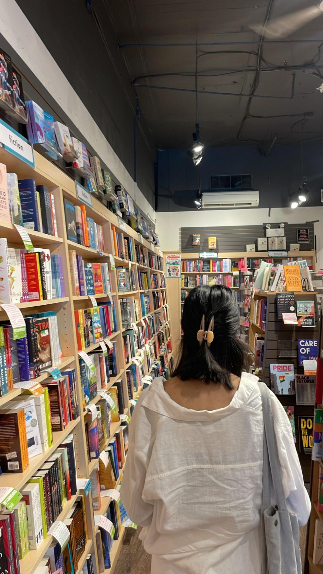 The back of a person walking through the aisle of a book shelf