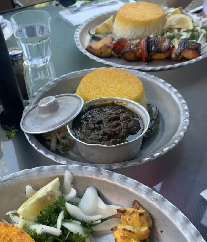 Ghormeh sabzi on a silver plate served with saffron rice with a side of lemons and onion.