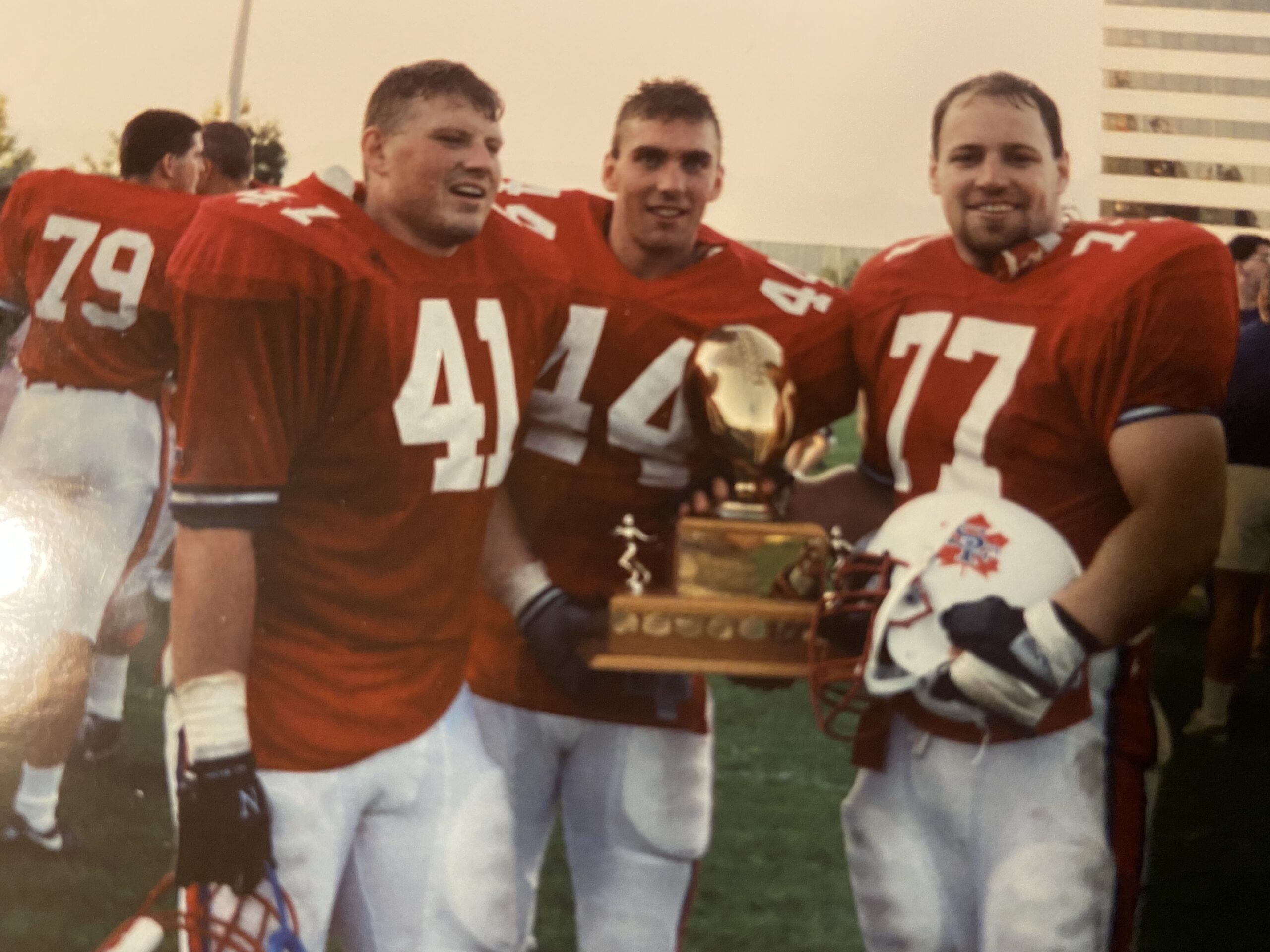 photo of Clayton holding the Shrum Bowl trophy on the field with teammates.
