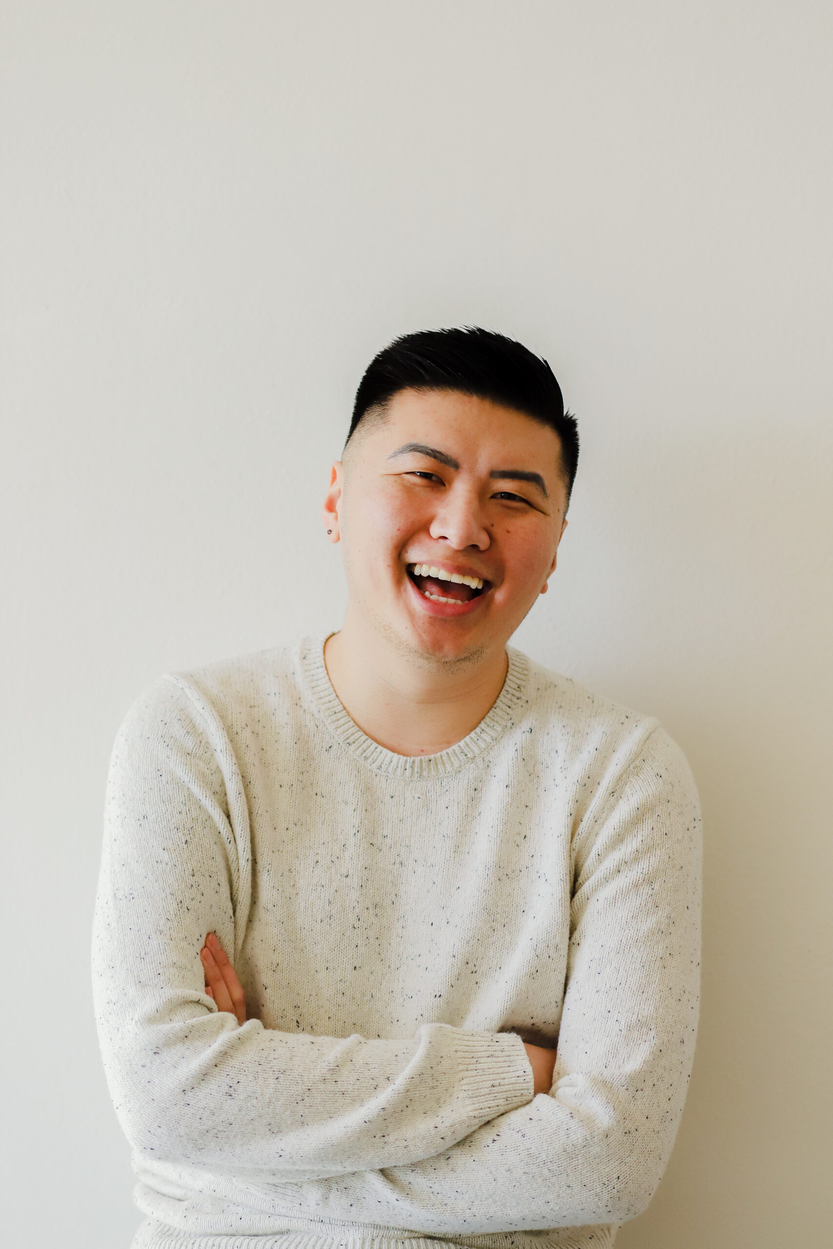 Headshot of David Ly in a white sweater with arms crossed and an open mouth smile