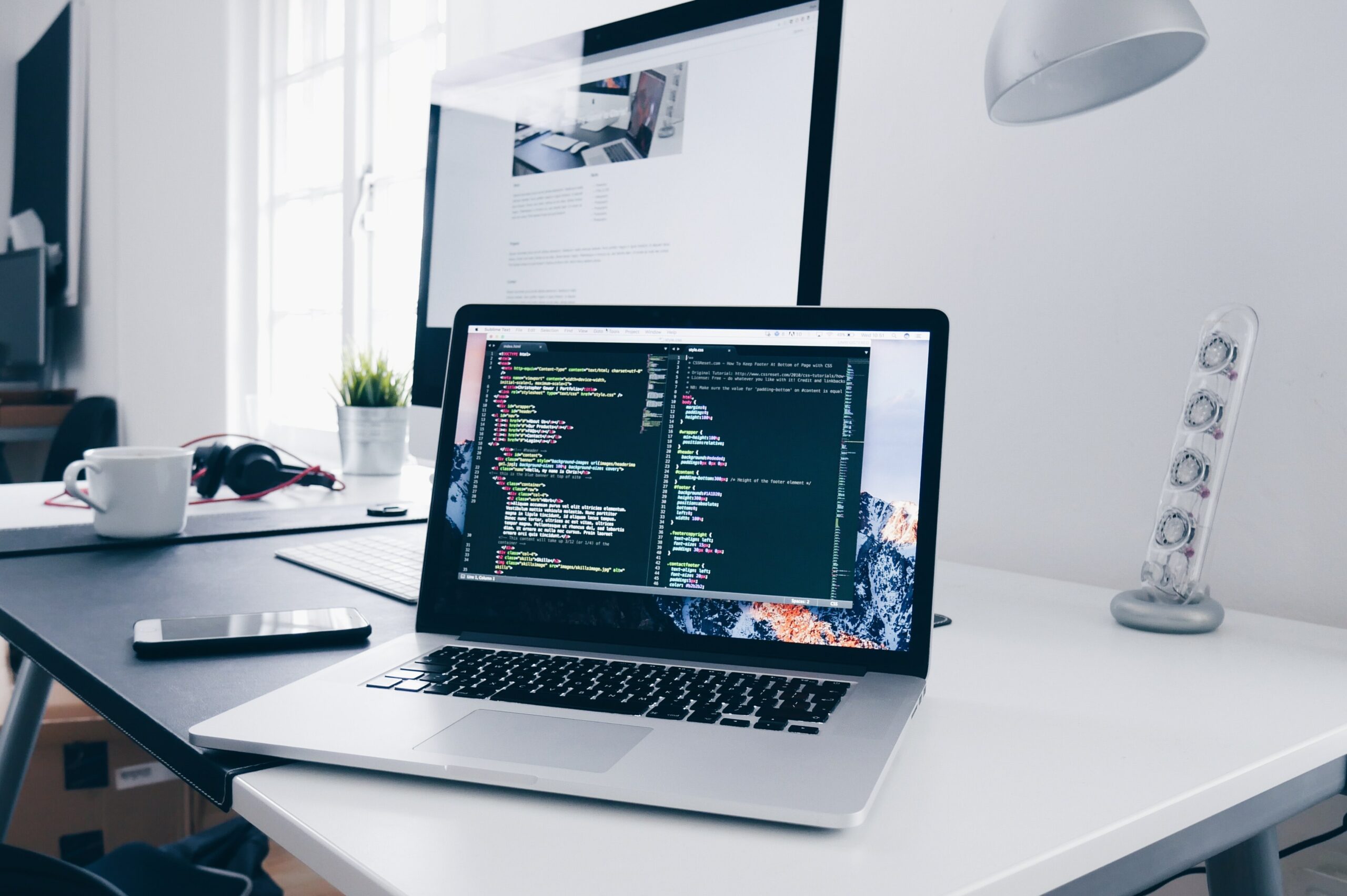 This photo is of a laptop sitting on a desk. The laptop screen has coding programming on it.