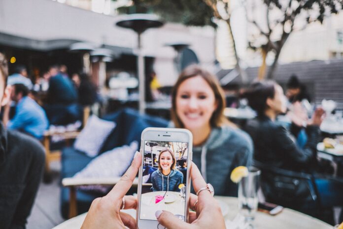 someone taking a cell phone photo of their friend at a restaurant table