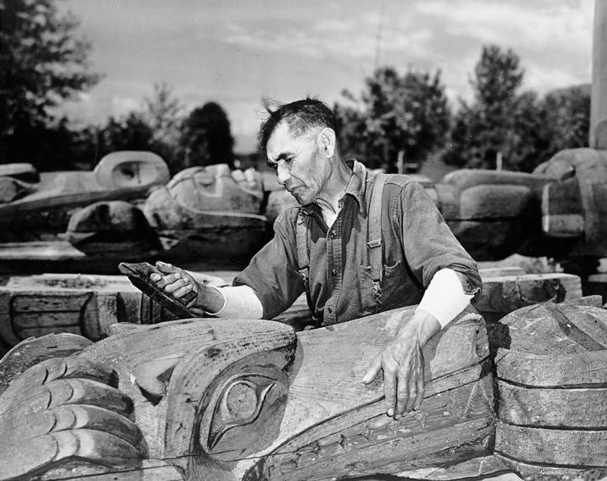 Black and white photo of Mungo Martin gazing down at a totem pole.