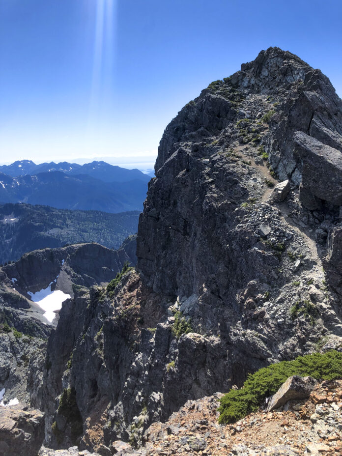 Photo of the horizon with a mountain peak on the forefront and a mountain range on the background.