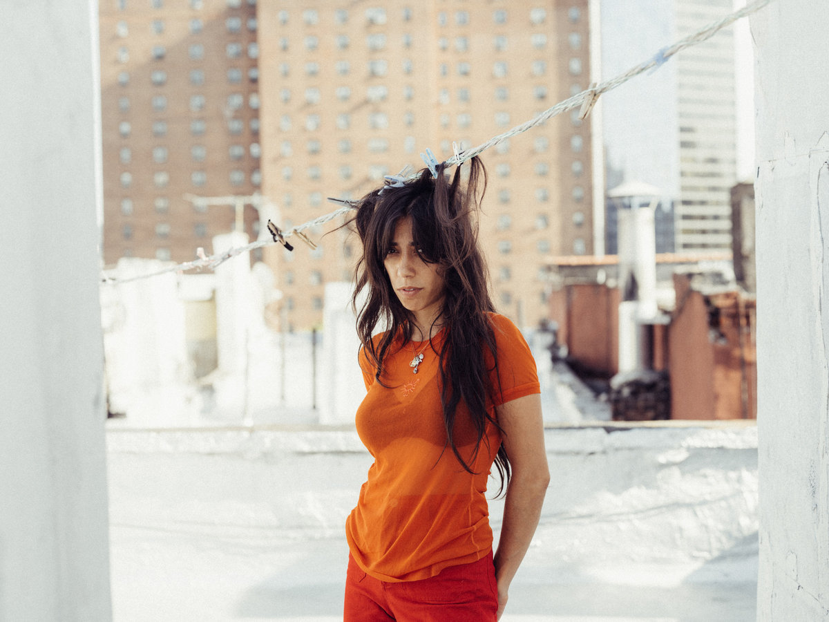 Rahill standing on a rooftop in a city wearing an orange shirt with her hair attached to a clothing line with pins.
