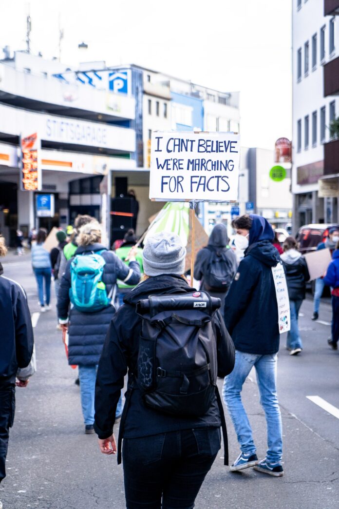 Photo of protesters marching, one of them is holding a sign that says "I can't believe we're marching for facts"