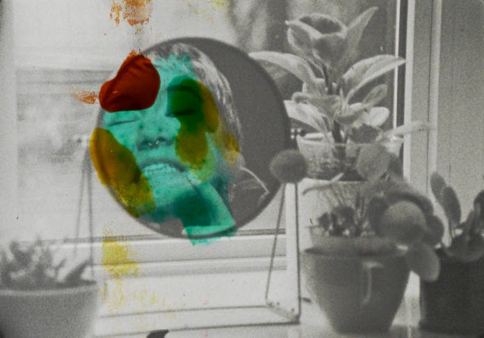 A person makes a playful face in the mirror, with her face painted bright colors and the rest of the photo is black and white