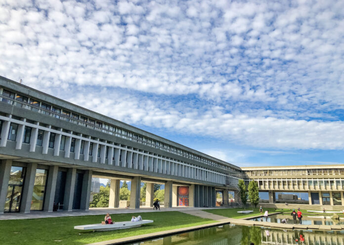This is a photo of the academic quadrangle at the SFU Burnaby campus. In front of the building is students sitting on the green grass.