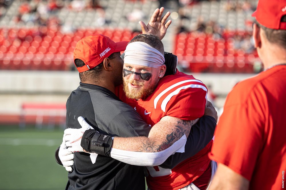 photo of head coach Mike Rigell hugging a player on the field.