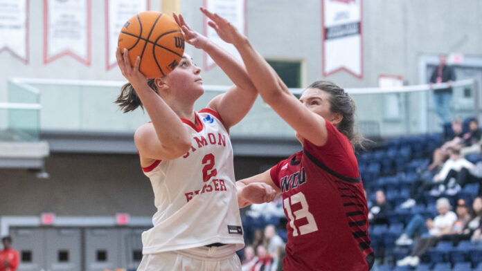 2023-01-12_BB-uniw-sfu-wou-by-wilson-wong_0435 Photo of an SFU women’s basketball player trying to get a shot off against an opponent.