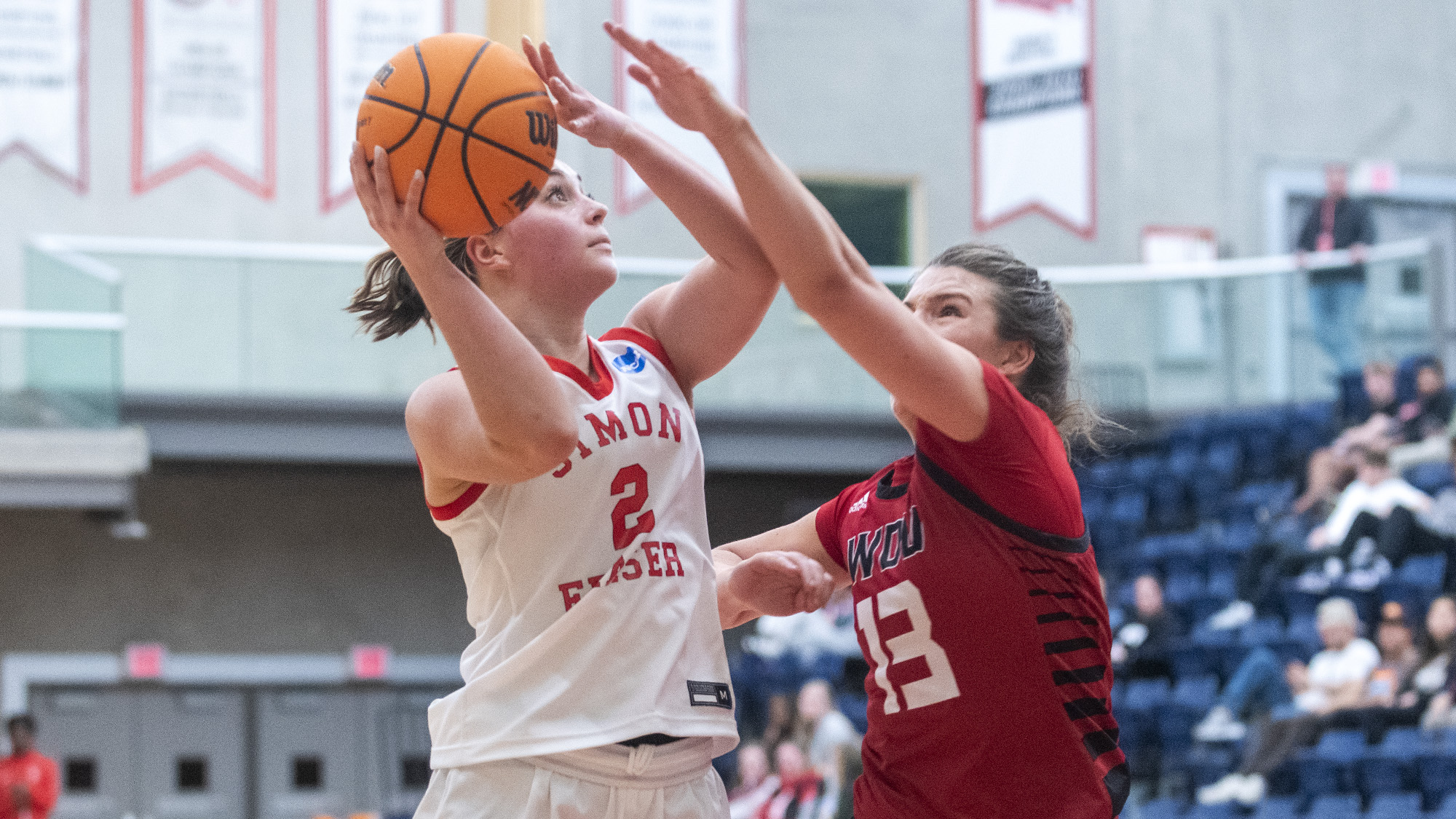 Photo of an SFU women’s basketball player trying to get a shot off against an opponent.