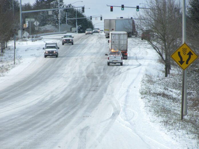 This photo is of snow covering the roads on a hill. A few cars are driving on the road and appear to be slipping on the road.