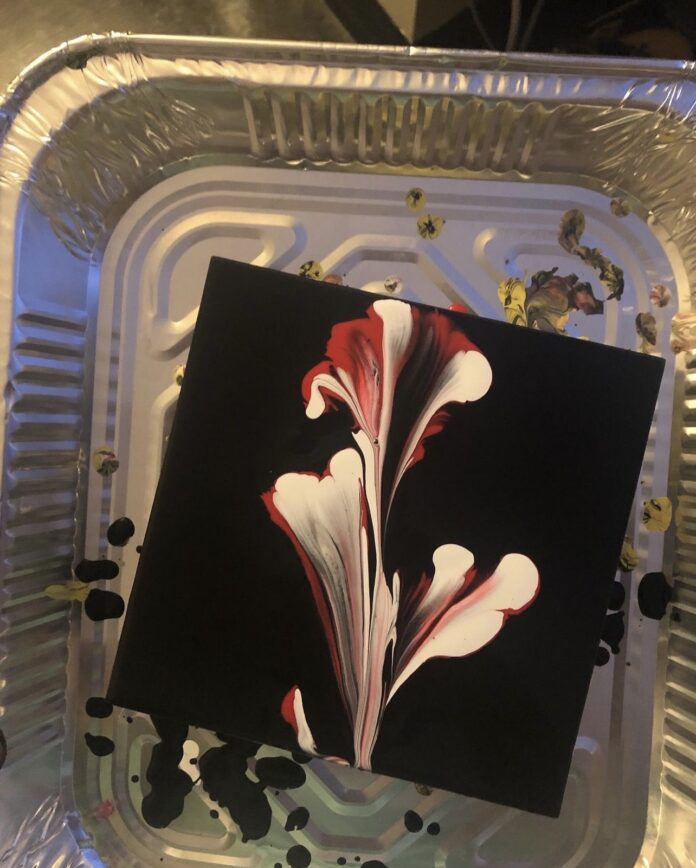 A white and pink flower on a black canvas background made using acrylic pour method.