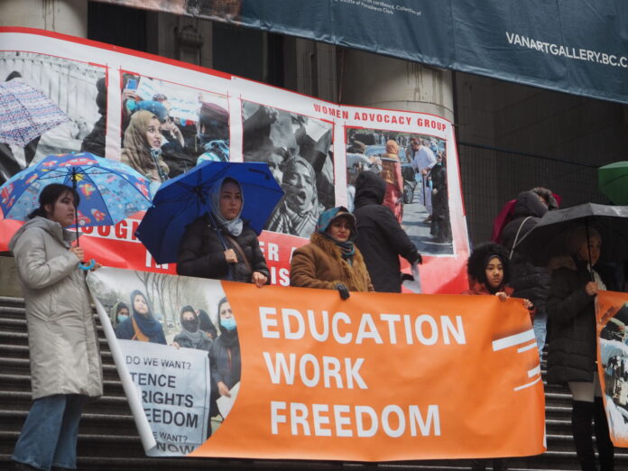 OLYMPUS DIGITAL CAMERA This is a photo of the protests outside of the Vancouver Art Gallery. The protestors are standing on the steps, holding a microphone, looking out to the crowd.