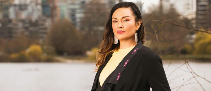 Closeup headshot of Angela Sterritt in front of blurred-out trees and buildings in the background.