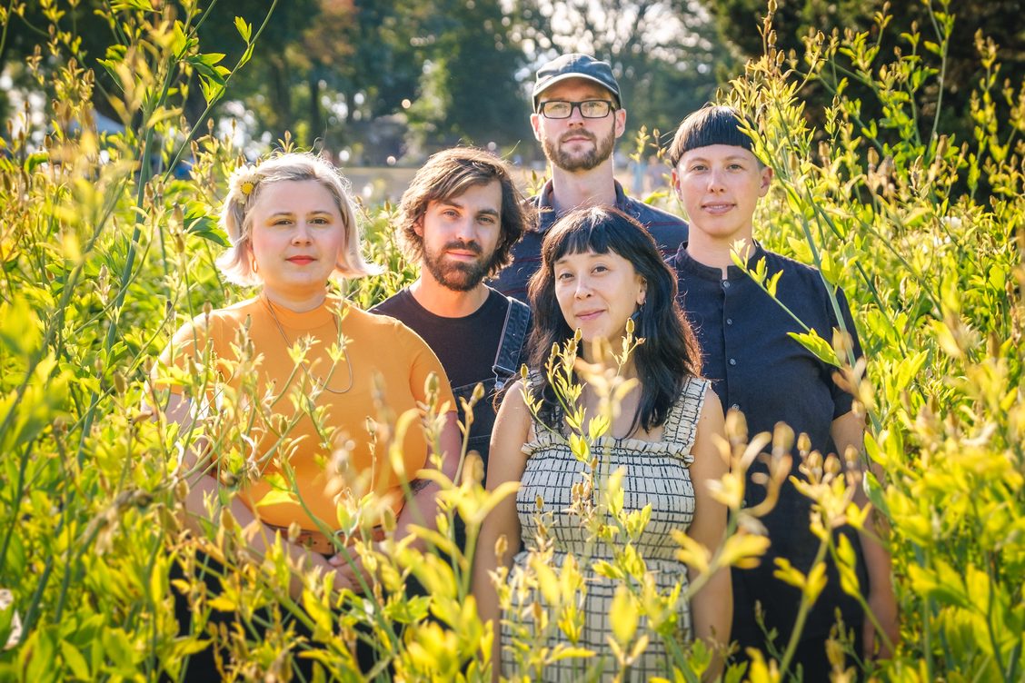 Group photo of Only a Visitor members surrounded by plants with flowers that are just about to bloom.