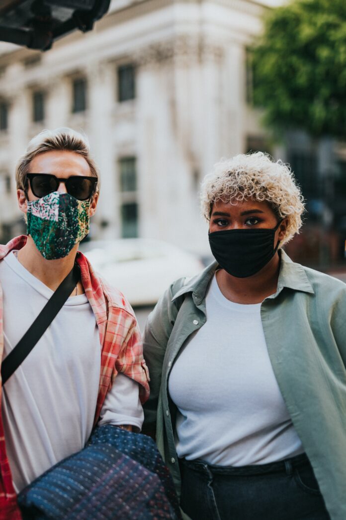 This is a photo of two individuals in masks. They are standing next to each other and looking into the camera. They can be seen from the waist up.