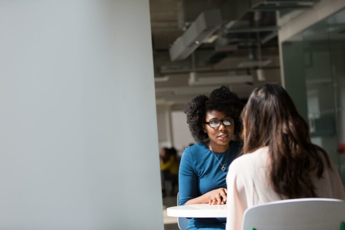 This is a photo of two individuals sitting at a table. They appear to be confiding in each other.