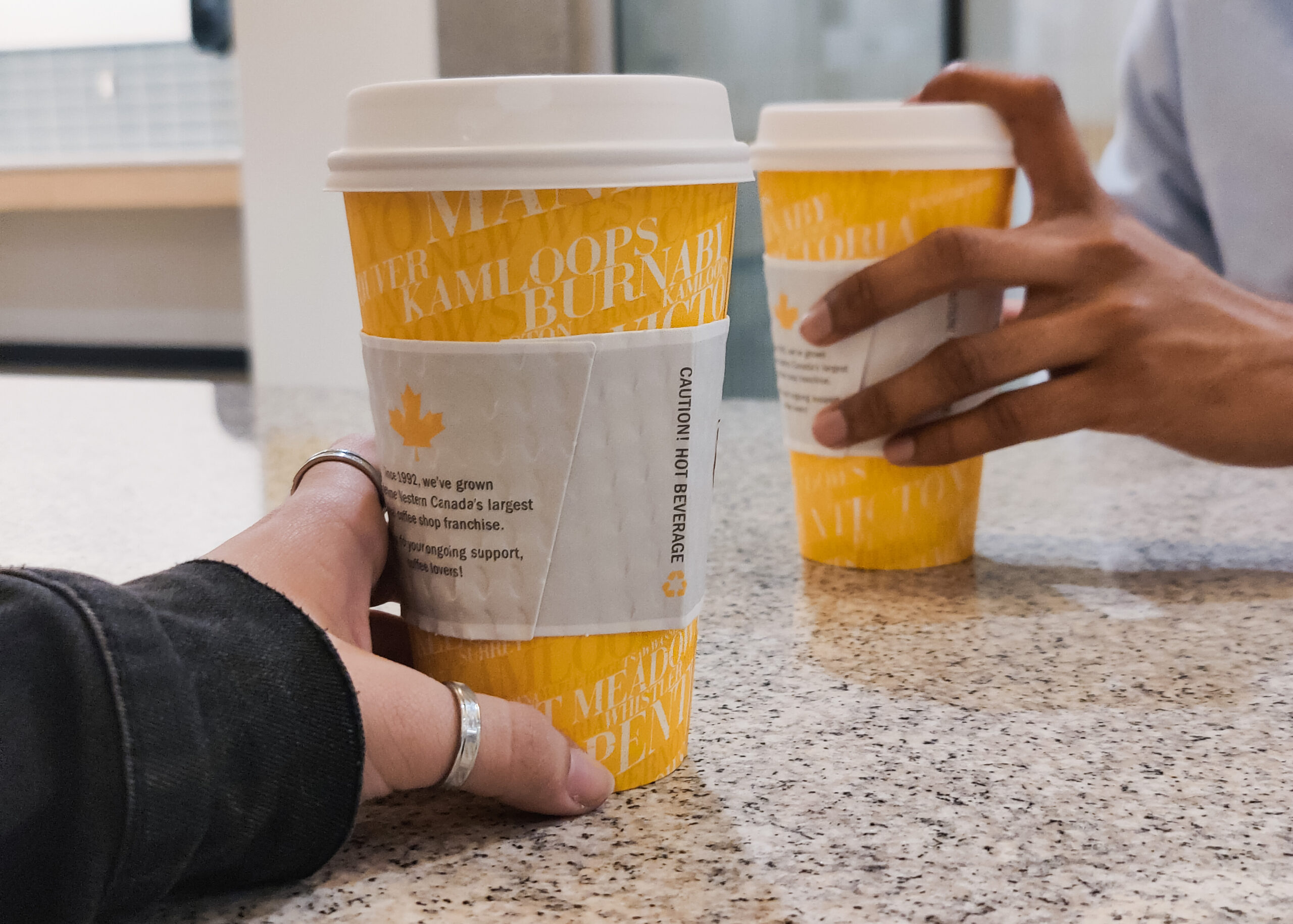 Two paper coffee cups being held by two individuals facing each other.