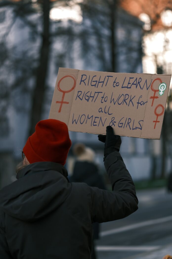 nk-ni-uDRctP-2qp8-unsplash This is a photo of an individual, with their back to the camera, holding a sign that reads “Right to Learn. Right to Work for all Women and Girls.”