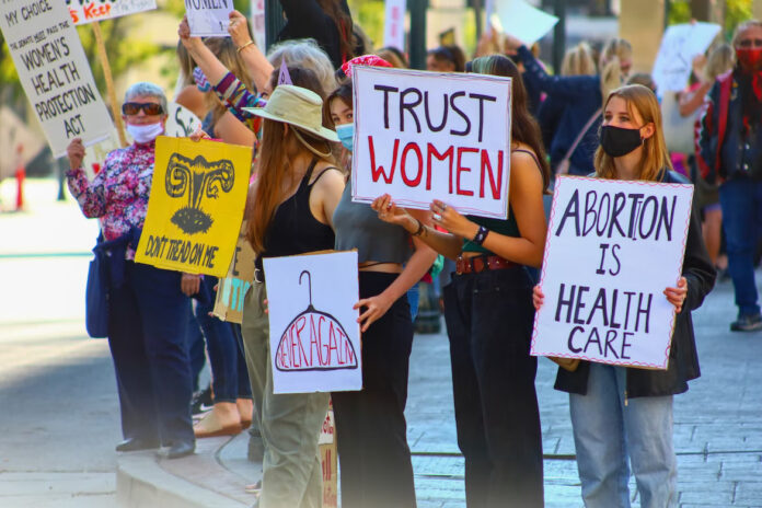 multiple people holding up abortion rights signs at a protest, including signs that read “abortion is healthcare” and “trust women”