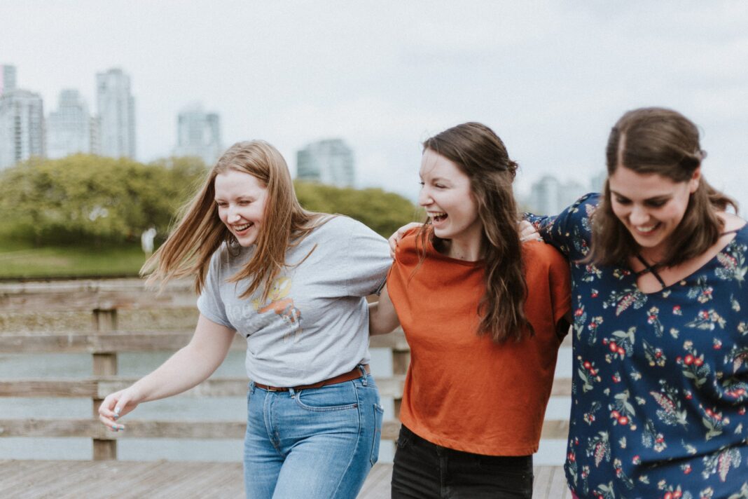 A photo of three women hugging and laughing with a city skyline as a background