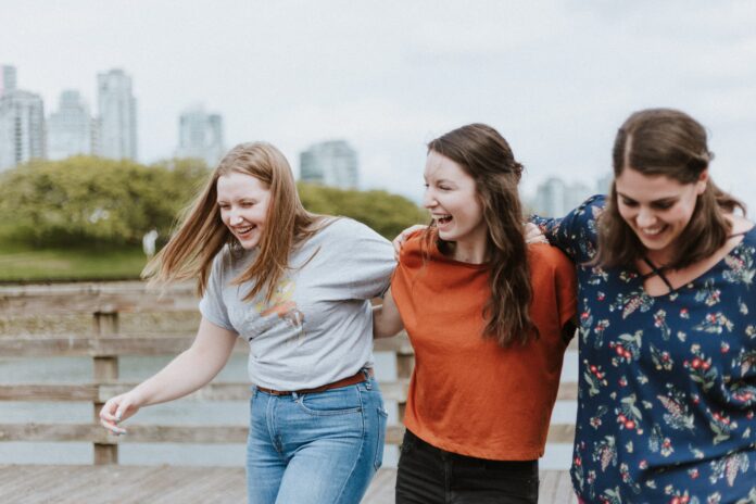 A photo of three women hugging and laughing with a city skyline as a background