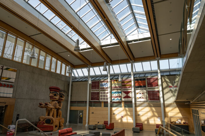 This is a photo of the SFU archaeology space at the Burnaby campus. There are chairs and tables lined up and a large totem pole near the wall