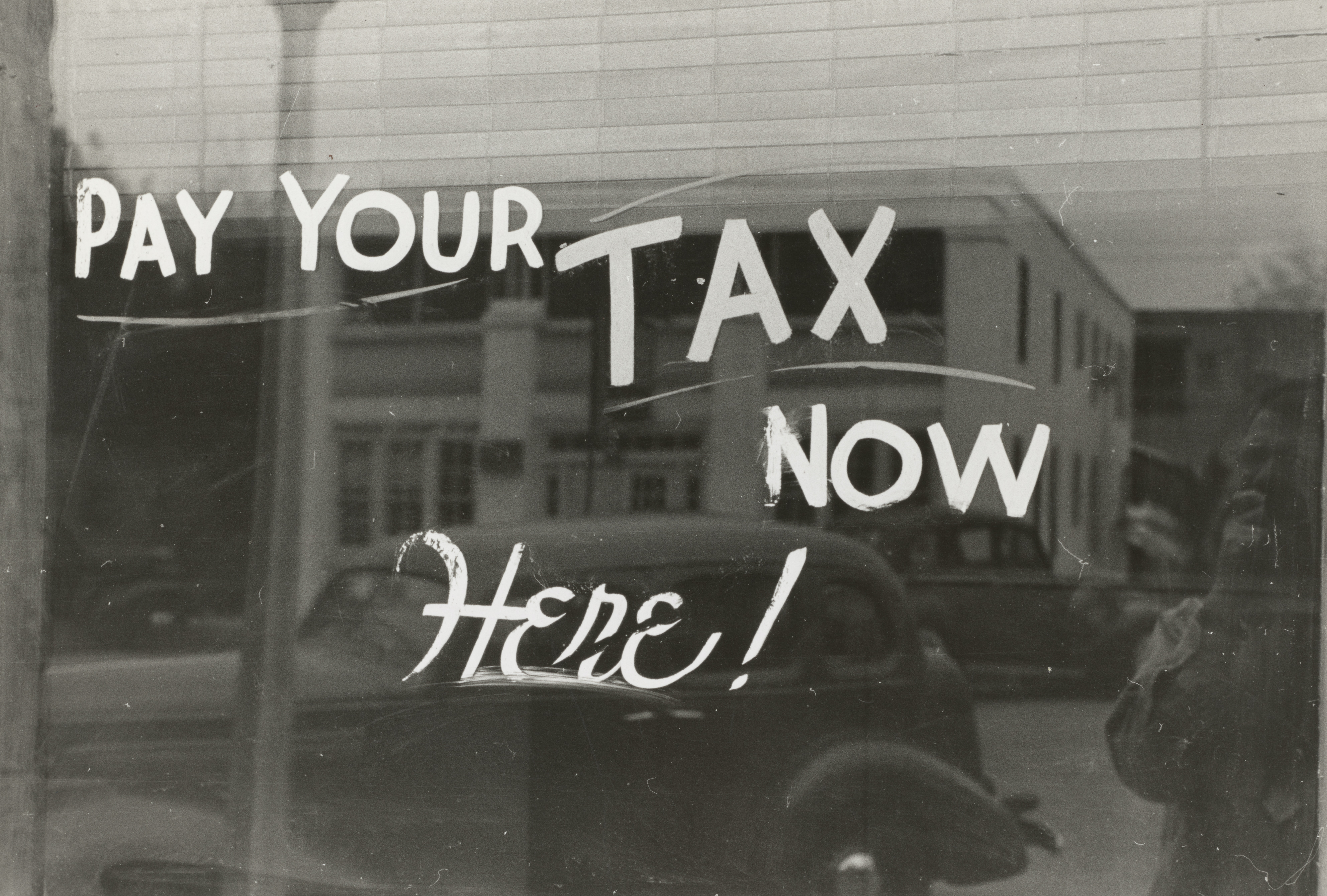 A window with white marking on it stating "Pay your tax now here!"