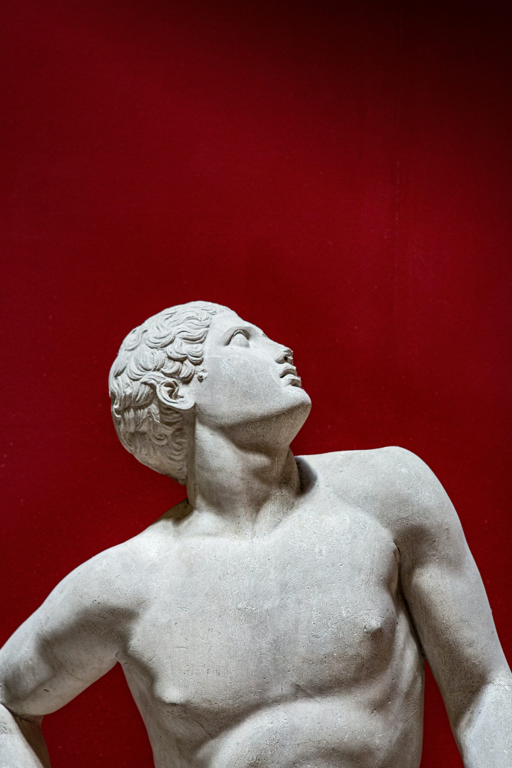 A human statue looking up behind a red background.