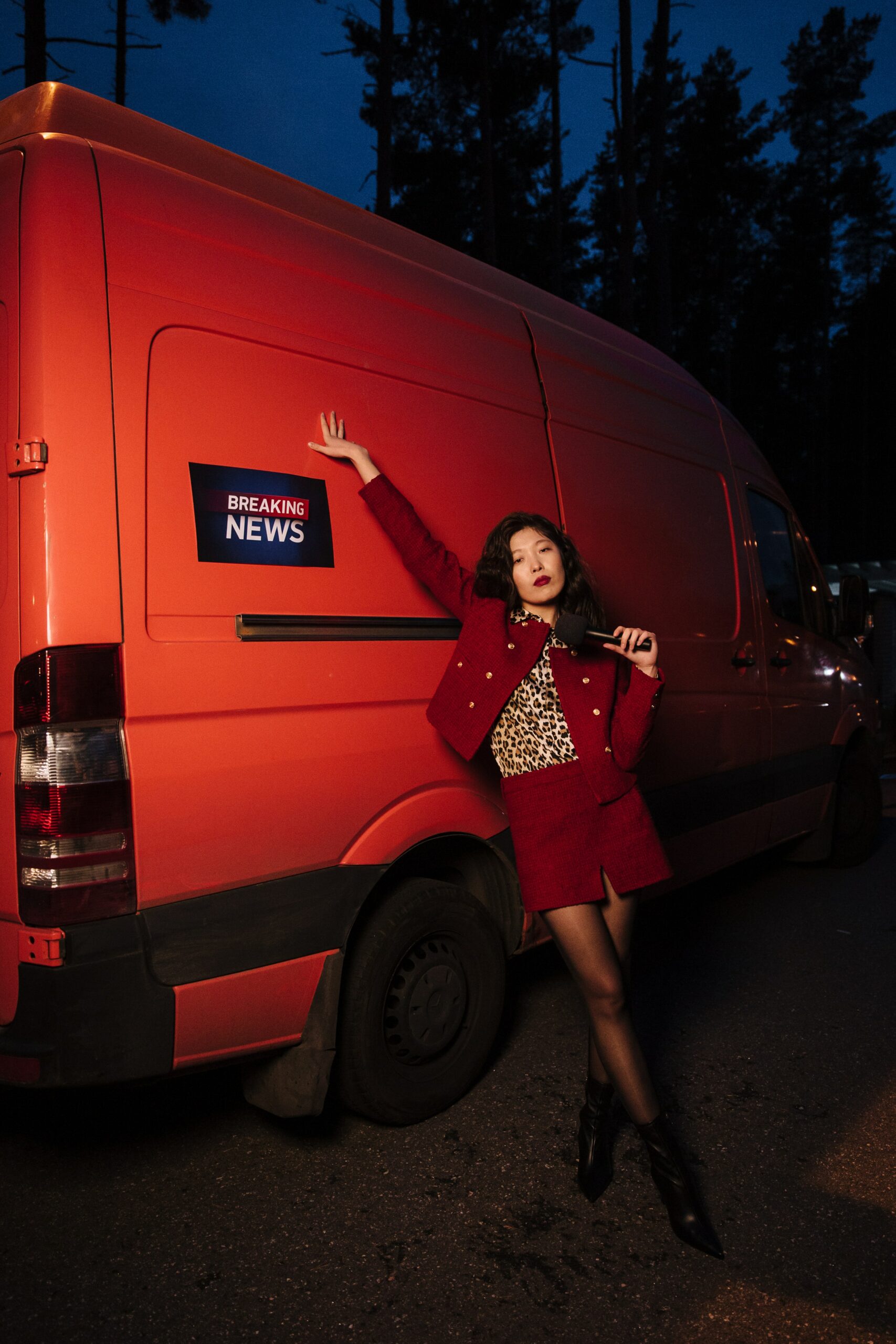 A woman in a red blazer and skirt standing near a news van