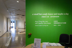 A photo of the entrance to the exhibit. The front wall is green and has the name of the exhibit and additional details in both English and Chinese alphabet. There is both a ramp and a small staircase leading down into the spacious exhibit.