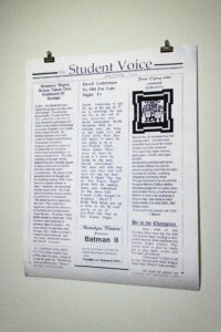  Photo of a large paper bulletin with printed text hung on the wall. The bulletin features three columns of articles with the headline “Student Voice.” The first column is an article written by Lam. The headline says “Womens’ rights group takes over the continent of Europe.”