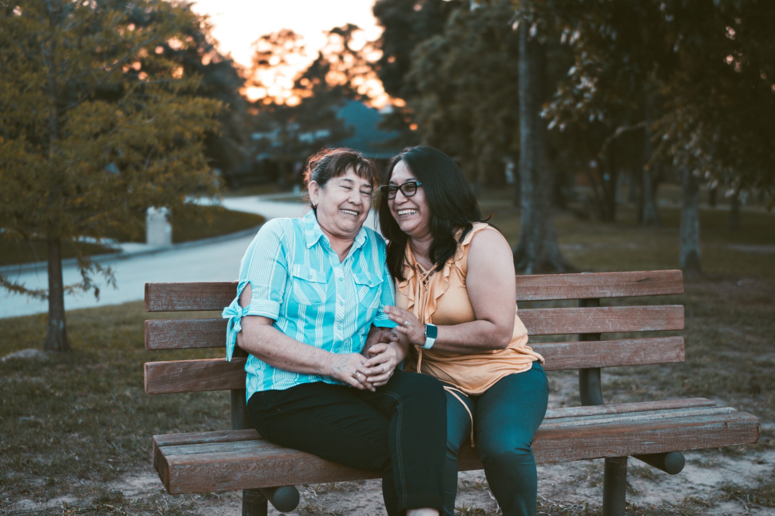 Two older women of colour laughing, while sitting on a park bench.