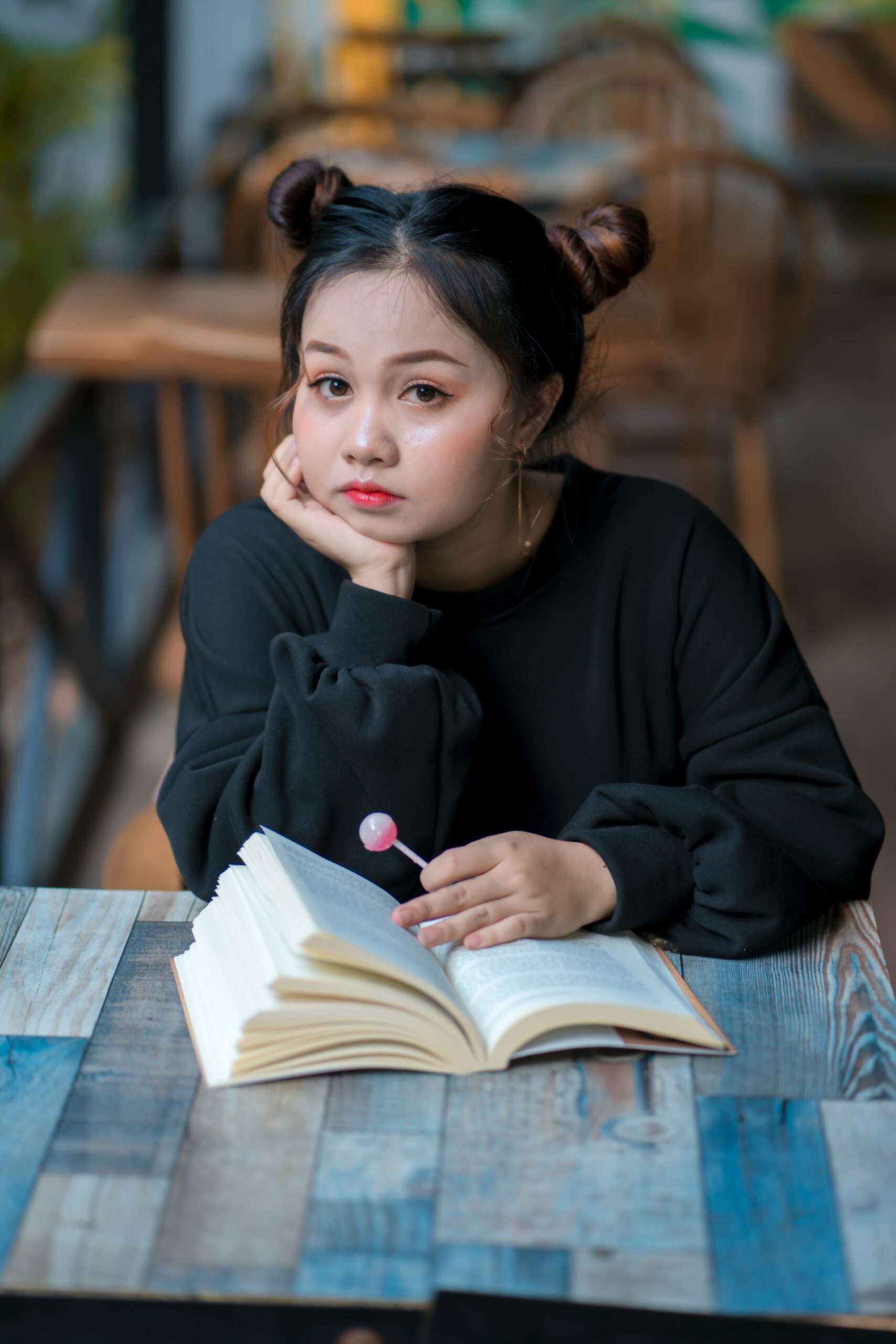 Pensive girl reading book in cafe holding a lollipop