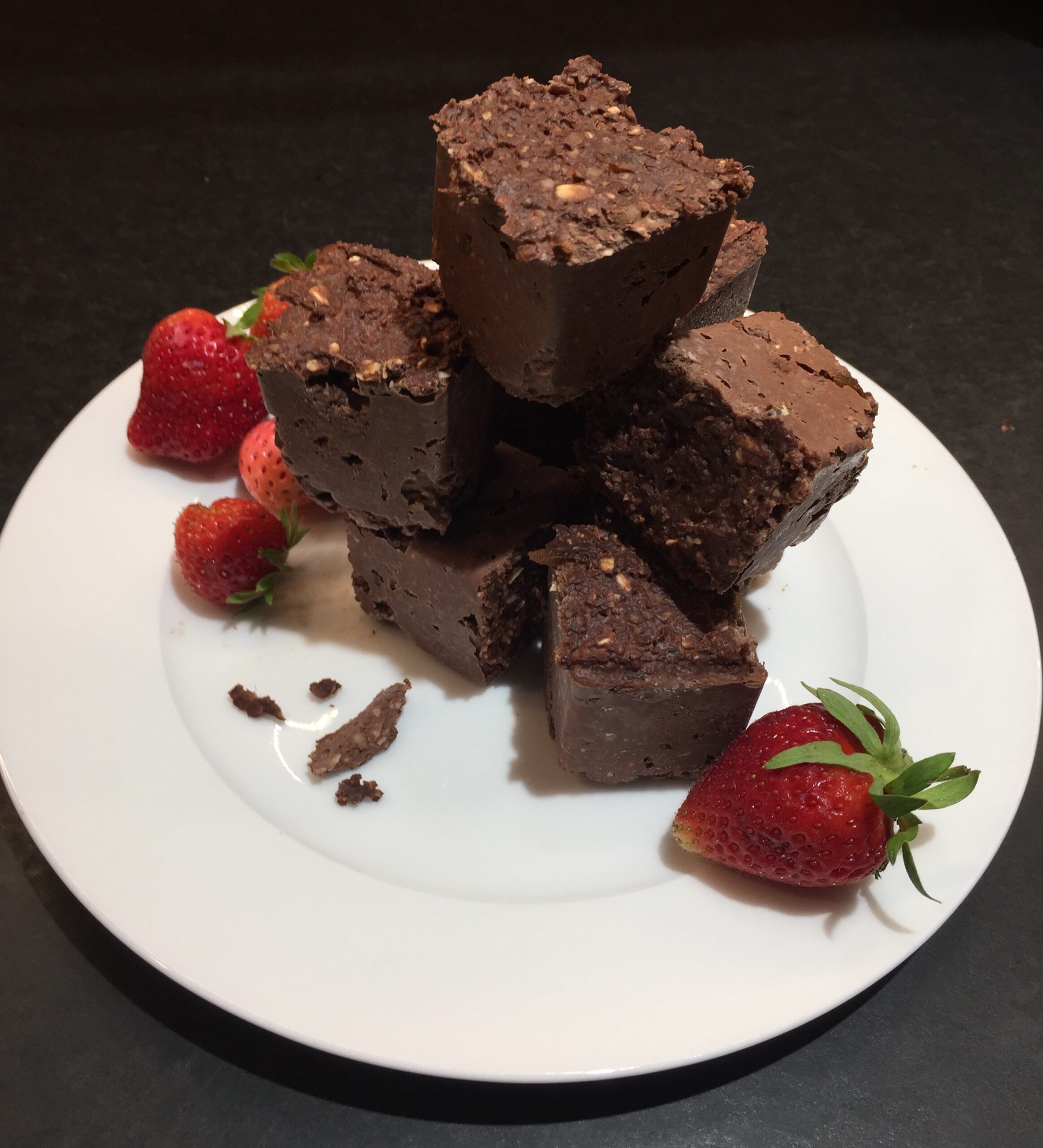 Brownie squares piled on top of each other tall on top of a white plate with strawberries on the side.