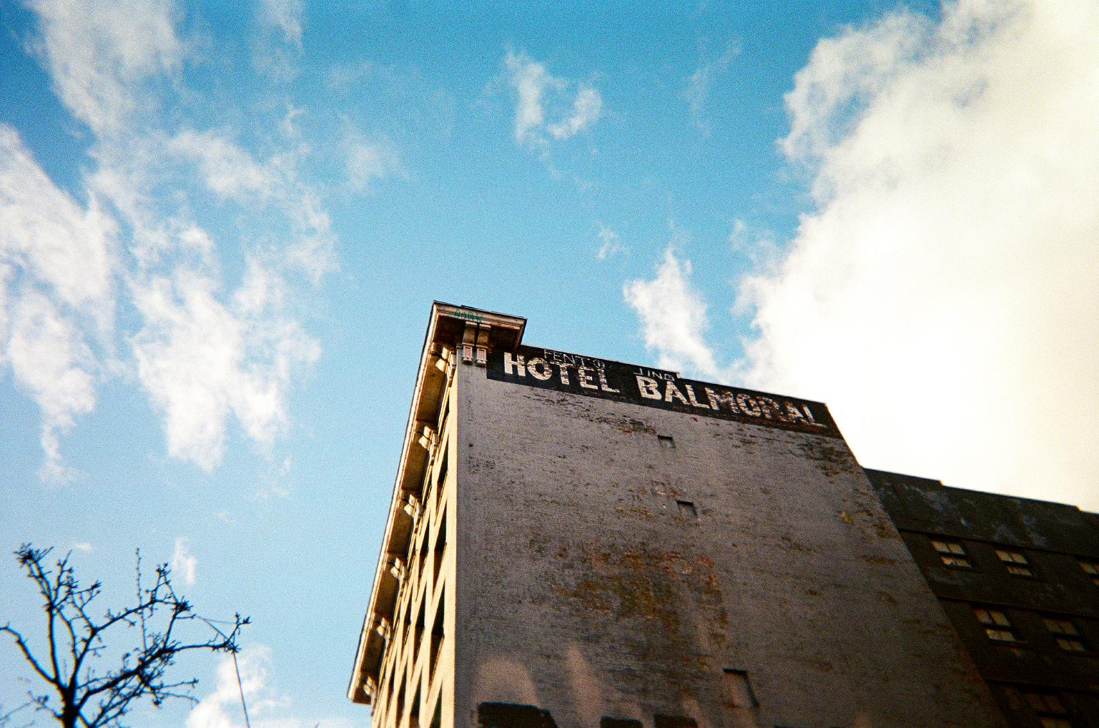 Photo from below looking up at a blue, cloudy sky and the side of a gray apartment with a sign that says “Hotel Balmoral”