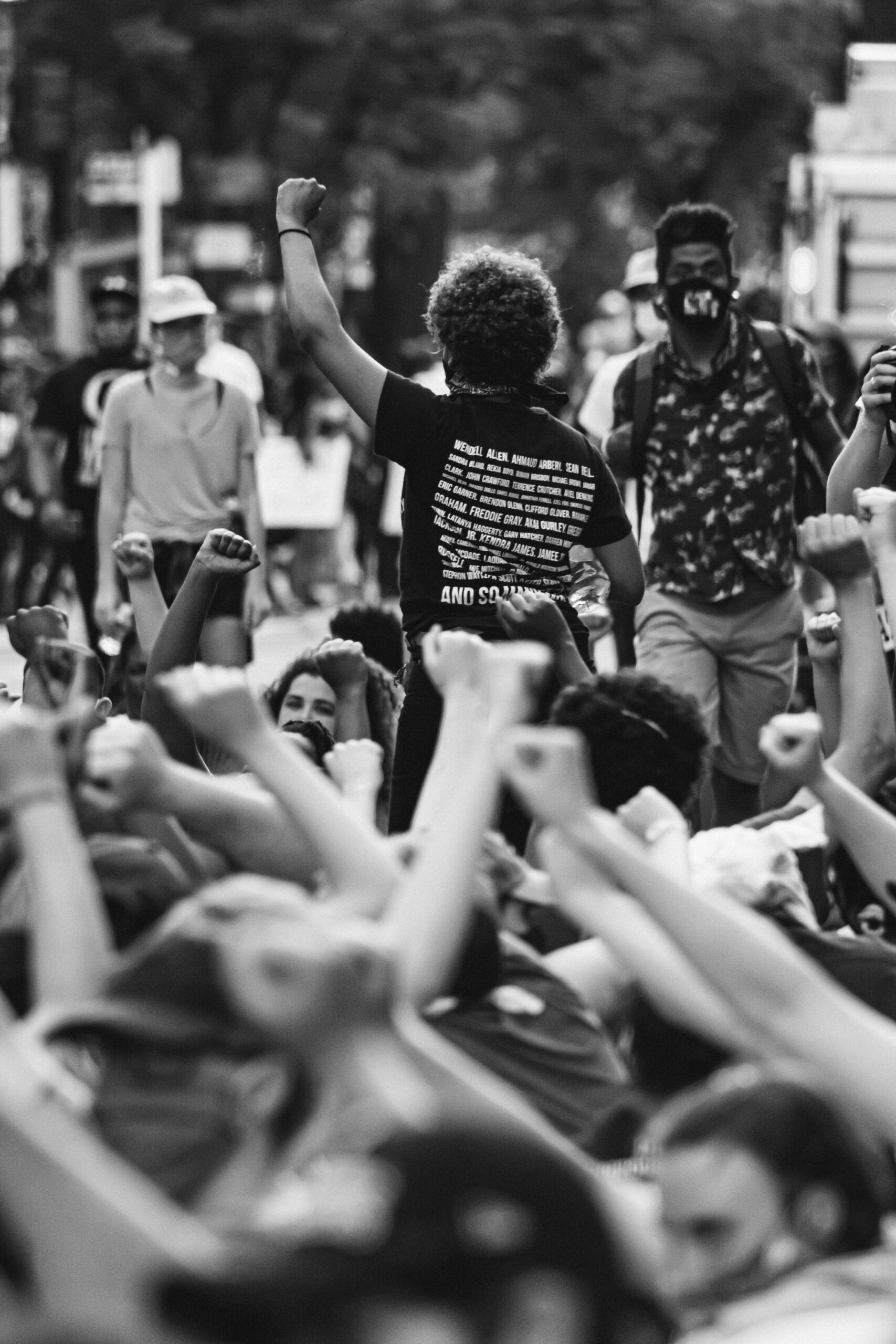 A black and white photo of a crowd of protestors with their fists in the air on the street taken from above.