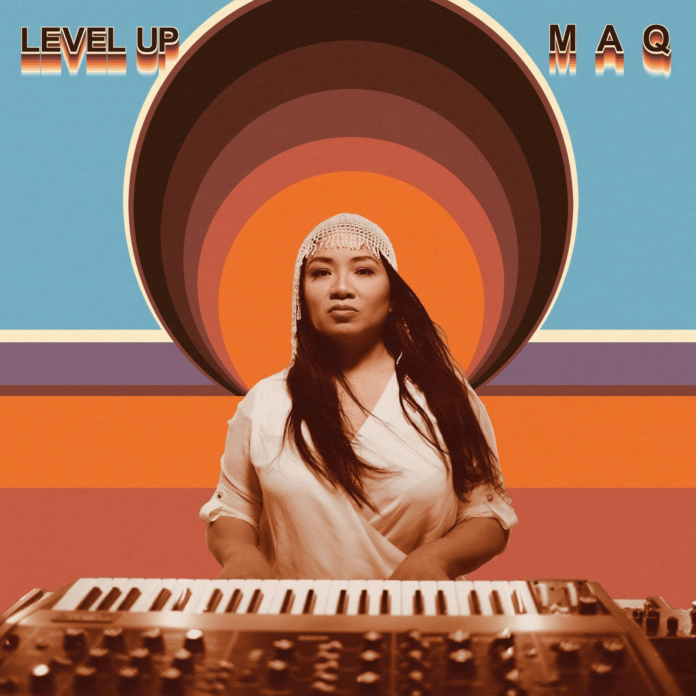 Album cover featuring a photo of Mary Ancheta behind a psychedelic background with a spiral with stripes, warm orange, blue, and purple. Ancheta is playing a keyboard and looking fiercely into the camera. She had long black hair, wearing a white headpiece and silky shirt.