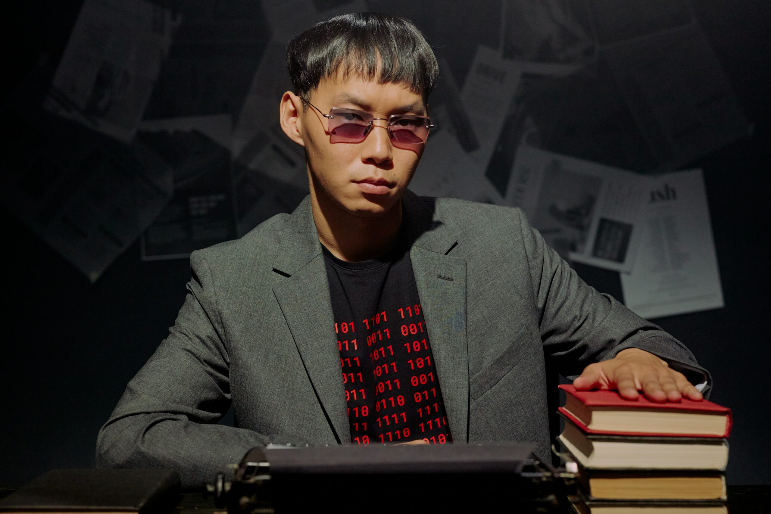 A man in a gray suit blazer sitting in front of a typewriter touching a red book