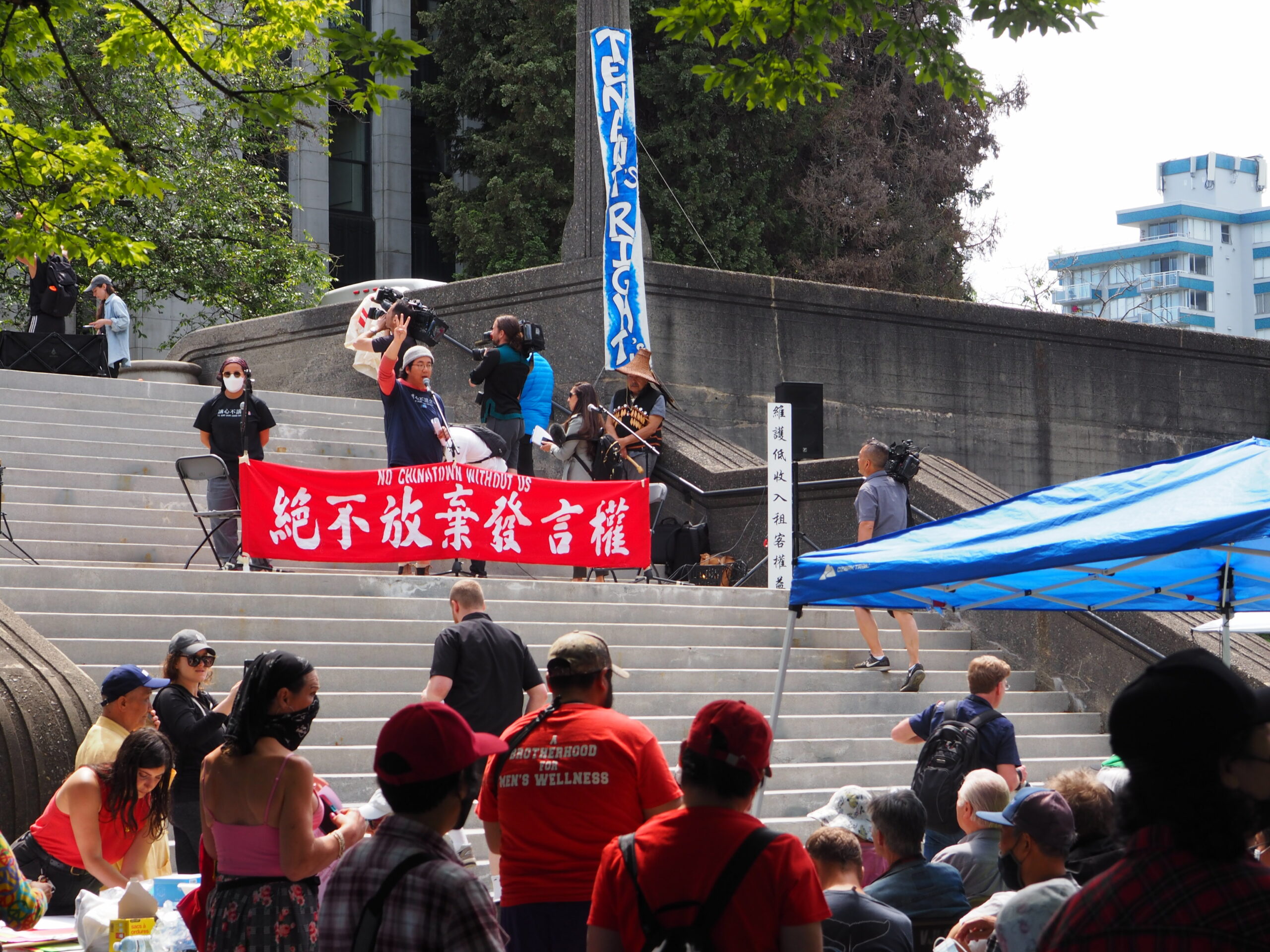 This is a photo of the rally held at the Vancouver Art Gallery. There are people on the steps of the gallery holding signs and speaking to a large crowd