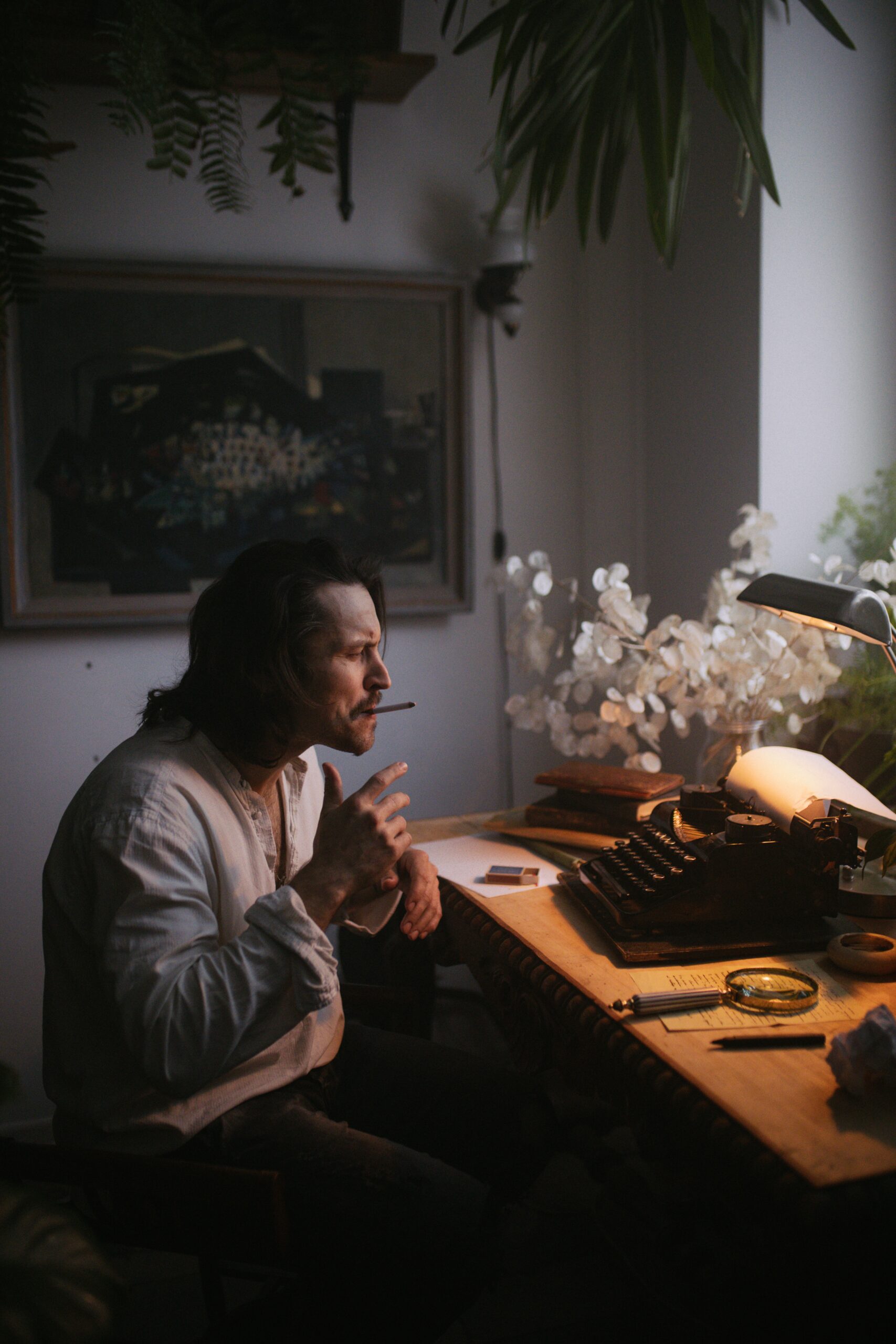 Novelist staring pensively at a typewriter while smoking a cigarette.