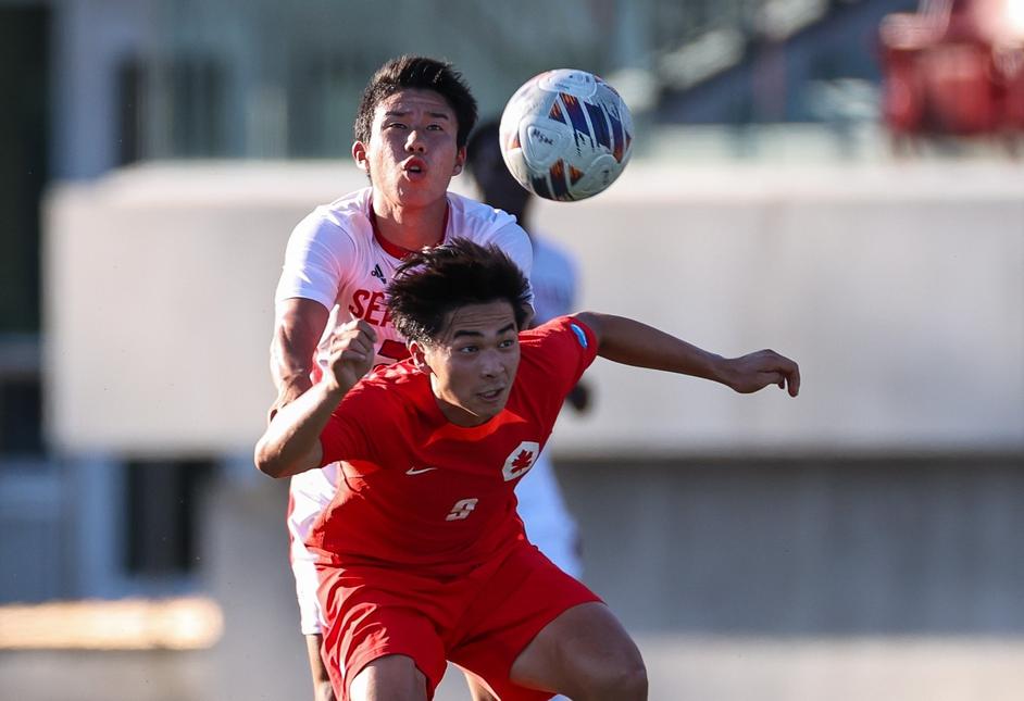 two soccer players captured jumping up to headbutt the ball