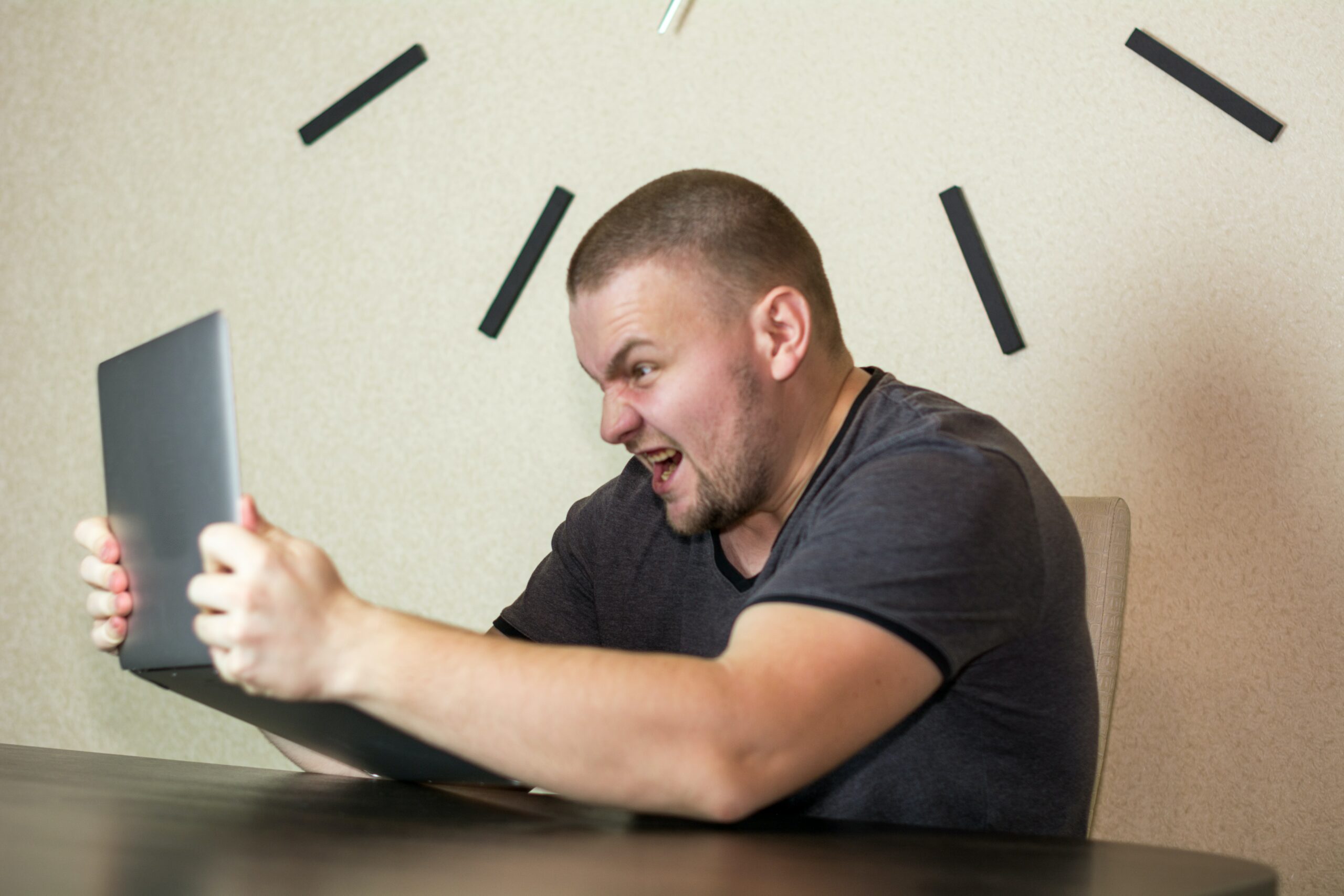 Angry man holding and yelling at a laptop.