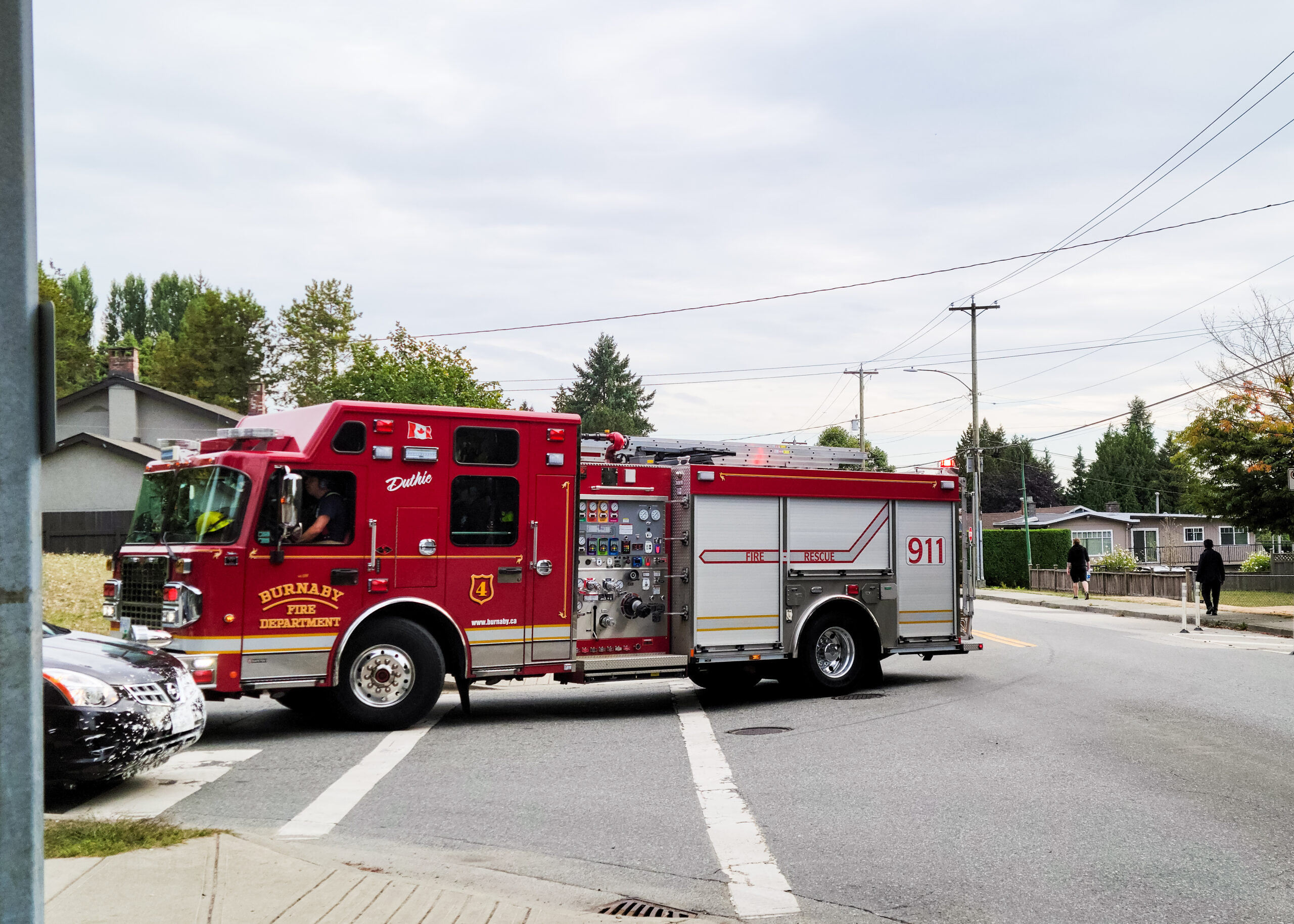 This is a photo of a City of Burnaby Firetruck. The truck is driving down the street, turning a corner. The emergency lights are not flashing.