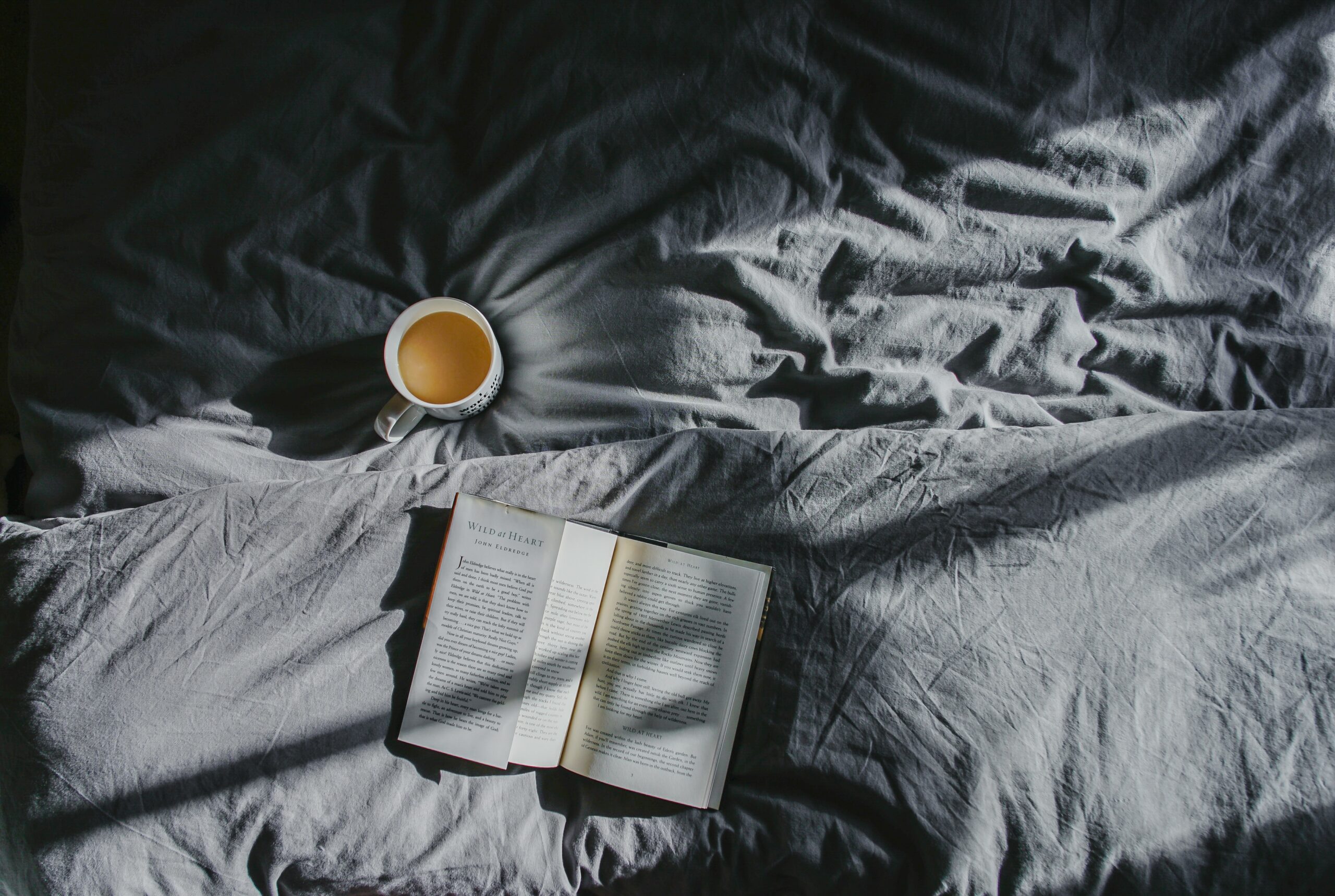 A white ceramic mug holding a liquid inside. A book is besided the mug, all resting on textiles.