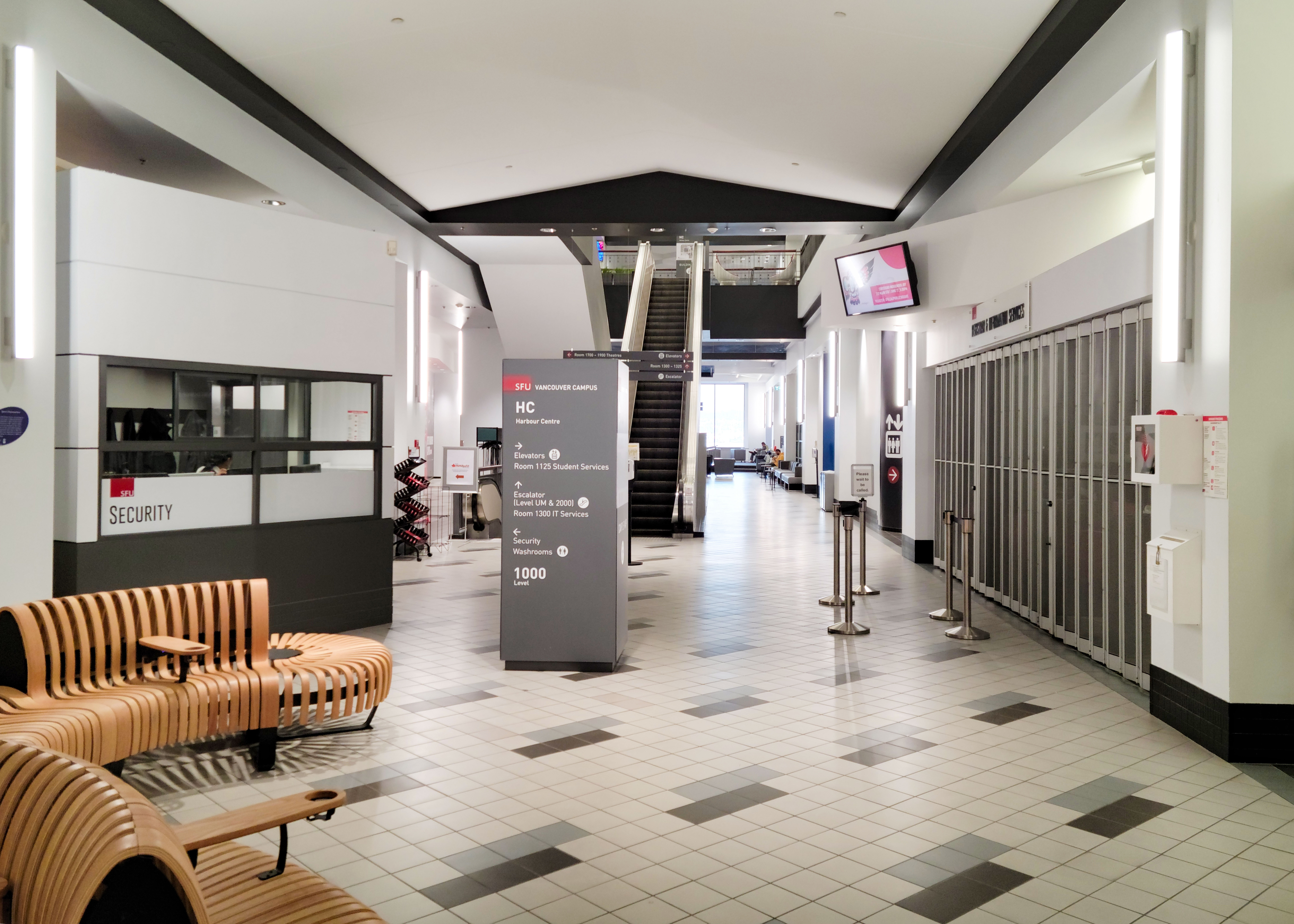 This is a photo of the SFU Vancouver campus. The lobby contains the security booth, seating for students to study, escalators, and a location directory.