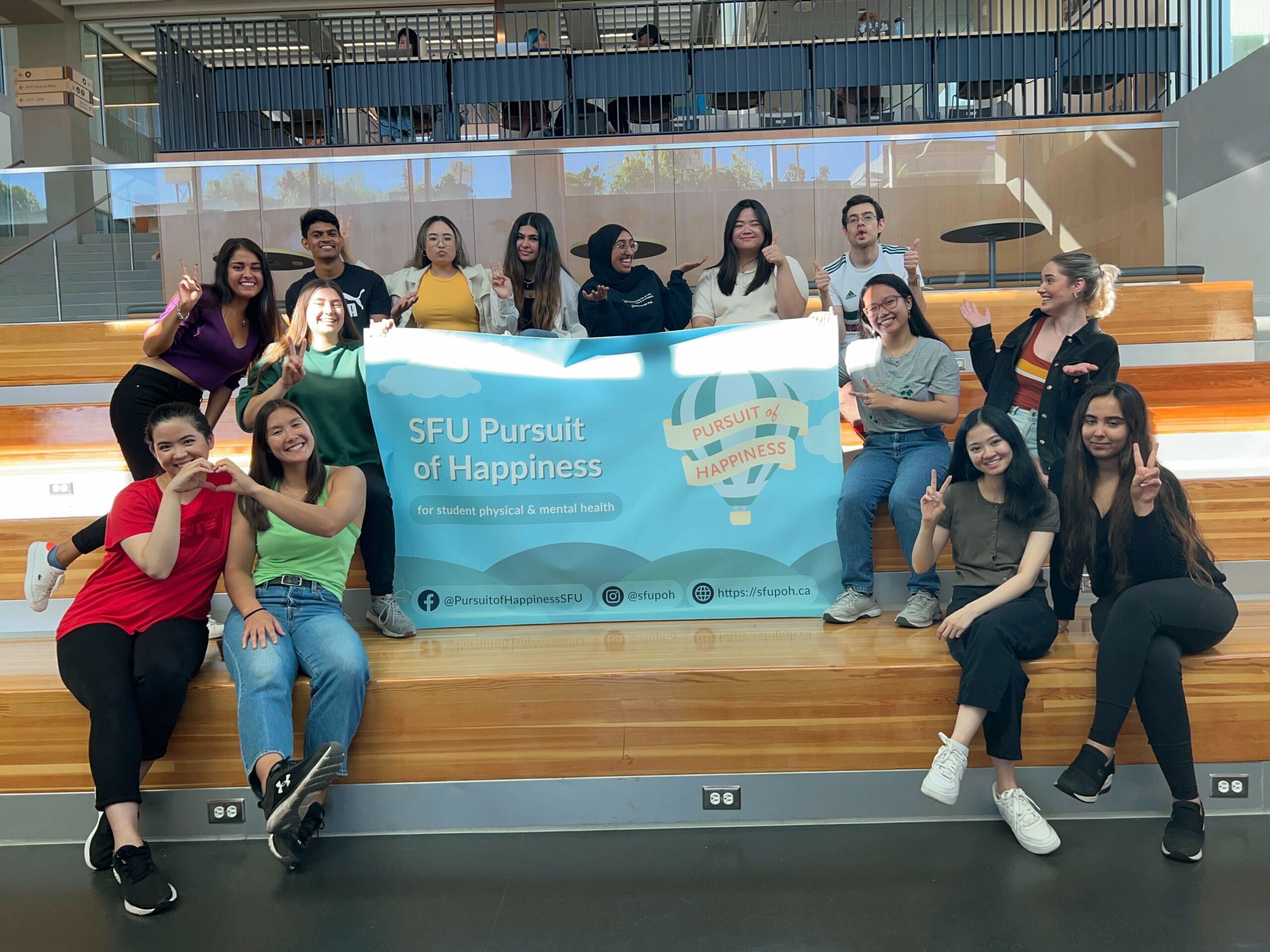 A photo of a group of young adults holding a sign reading “SFU Pursuit of Happiness.”